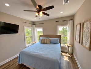 Une chambre à coucher avec un lit, un ventilateur de plafond, une télévision et de grandes fenêtres.