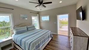 A bedroom with a bed, a nightstand, a dresser, a ceiling fan, and a TV mounted on the wall.