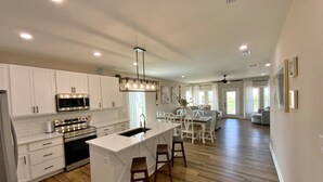 A spacious kitchen with white cabinets, a central island, and a dining area with a high ceiling and pendant lighting.