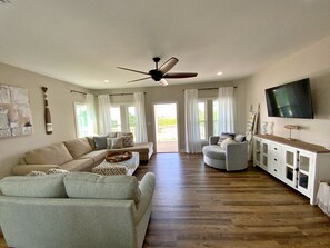 Relax in this spacious living area with a high ceiling and ceiling fan, featuring a large window with a view of the outdoors.