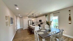 A spacious kitchen with white cabinets, a central island, and a dining area with a wooden table and white chairs.