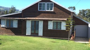 A two-story wooden house with a sloped roof, a front porch, and a garage. - Villa de Charme à Bois Court (10 people) (Le Tampon)