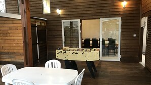 A wooden-floored room with a foosball table, white chairs, and a glass door leading to a dining area. - Villa de Charme à Bois Court (10 people) (Le Tampon)