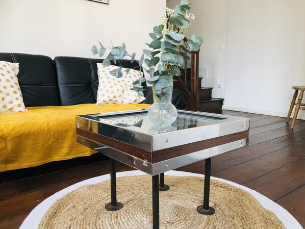 Un salon avec une table basse en verre, un canapé jaune et un divan en cuir noir.