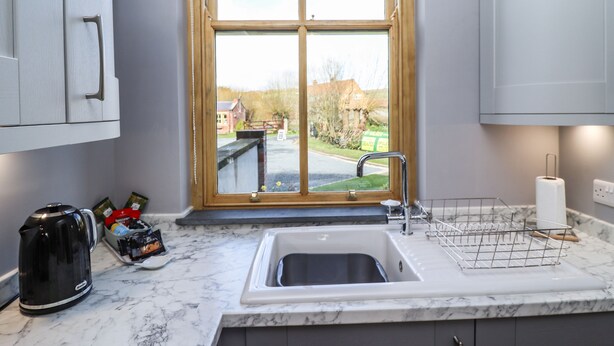 A kitchen with a sink, a kettle, and a window with a view of a street and houses.