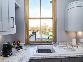 A kitchen with a sink, a kettle, and a window with a view of a street and houses.