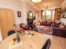 A dining area with a round wooden table, leather chairs, and a red patterned rug.