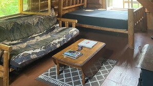 A log cabin interior with a loft bedroom, a sofa, a coffee table, and a staircase. - Snowshoe Cabin - Spacious Rustic Retreat w/ Loft (Stony River Township)