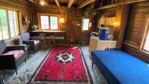 Interior de uma cabana de troncos com sala de jantar, cozinha e área de dormir.