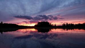 Um lago tranquilo ao pôr do sol, com o perfil das árvores e uma pequena ilha ao longe.