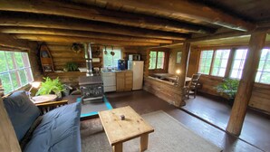 Een rustiek houten interieur met een bank, een kleintje tafeltje, een keuken met fornuis en een eettafel.