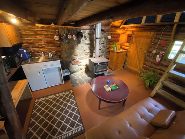 A cozy cabin interior with a stone wall, wooden furniture, a small kitchenette, and a fireplace.