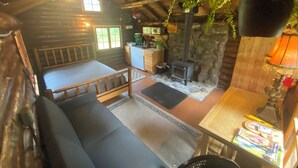 Ein gemütliches Blockhaus-Interieur mit einem Bett, einem Kamin aus Stein, einer Küchenzeile und einem hängenden Farn.