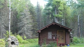 Eine kleine Holzhütte mit einem nahegelegenen Steinbau, umgeben von dichtem Wald.
