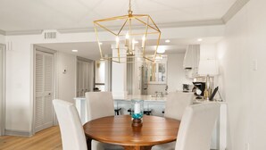 Un comedor con una mesa redonda de madera, cuatro sillas, una araña y una cocina al fondo.