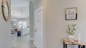 A hallway leading to a kitchen with a white door, a wooden-framed mirror, pendant lights, and a framed inspirational quote on the wall. - New Tucked Away Quiet Beach Haven (Little River)