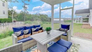 A covered patio area with wicker furniture, a table, and a view of the surrounding landscape. - New Tucked Away Quiet Beach Haven (Little River)