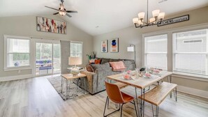 A spacious living room with a gray sofa, a dining table with chairs, a ceiling fan, and artwork on the walls. - New Tucked Away Quiet Beach Haven (Little River)
