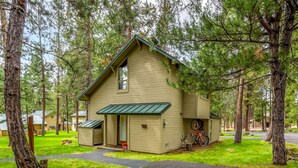 Une petite cabane à un seul étage, dotée d’un toit vert et d’une véranda, entourée d’arbres.