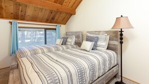 Une chambre avec un plafond en bois, un grand lit avec une literie à motifs, une lampe sur pied et une fenêtre avec des rideaux bleus.
