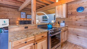 Une cuisine rustique dans une cabane en bois, dotée de plans de travail en granit, d’une cuisinière et d’armoires en bois.
