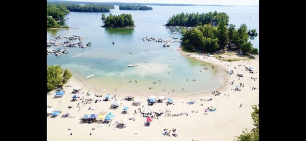 A beach with numerous tents and people, surrounded by water and trees.