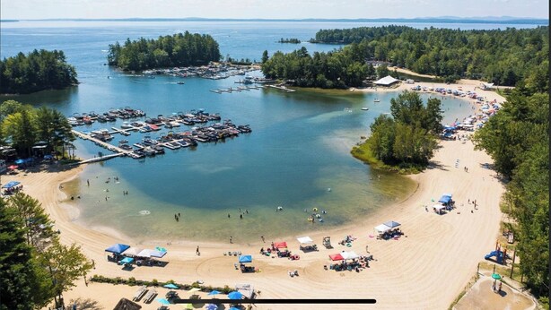 Uma praia com águas cristalinas, um porto de iates e uma área arborizada.