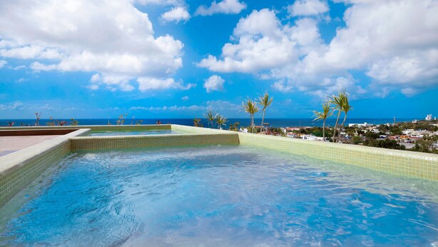 A pool with clear blue water, surrounded by tiled edges, and palm trees. - Heart of Cozumel w/ Rooftop Pool DC 501 (San Miguel de Cozumel)