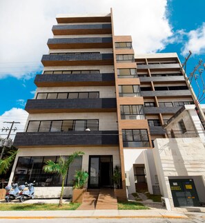 A multi-story building with a modern architectural design, featuring a combination of brick and wood paneling, large windows, and a visible entrance with steps leading up to the door.