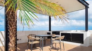 An outdoor patio with a table and chairs, a grill, and a view of the sky. - Heart of Cozumel w/ Rooftop Pool DC 501 (San Miguel de Cozumel)