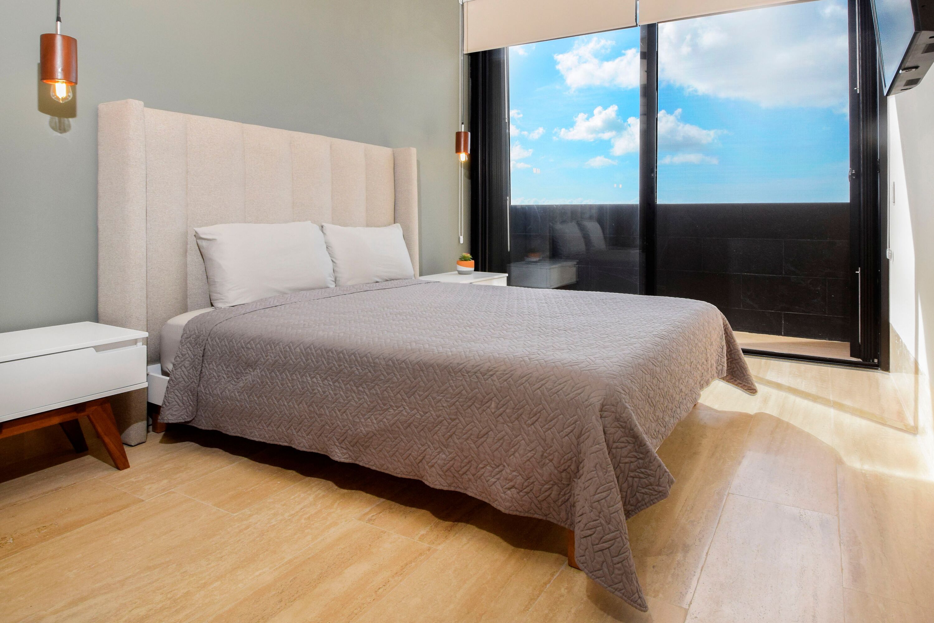 Un dormitorio moderno con una cama grande, una mesita de noche y vistas al cielo a través de un amplio ventanal.