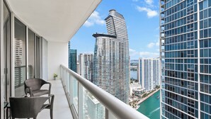 A balcony with a wicker chair, a view of a tall building, and a body of water. - 0142 Skyline Serenity 1B/1B (Miami)