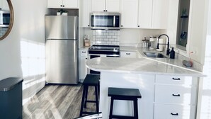 A modern kitchen with white cabinetry, stainless steel appliances, a marble countertop, and a built-in island with stools.