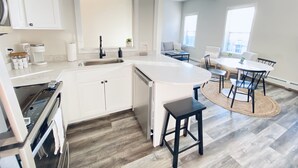 A modern kitchen with white cabinets, a built-in dishwasher, and a large island with stools.