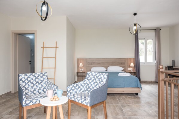 A bedroom with a bed, two patterned chairs, a small table, a ladder, and a desk with a chair.
