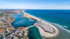 Vista aérea de uma área costeira com uma praia, um estacionamento e um rio.