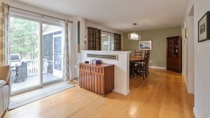 Uma sala ampla com porta de vidro deslizante para um pátio, um armário de madeira, uma mesa de jantar com cadeiras e um quadro pendurado na parede.