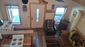 A cozy cabin interior with a wooden ceiling, a fireplace, a dining table, a couch, and a kitchen area.