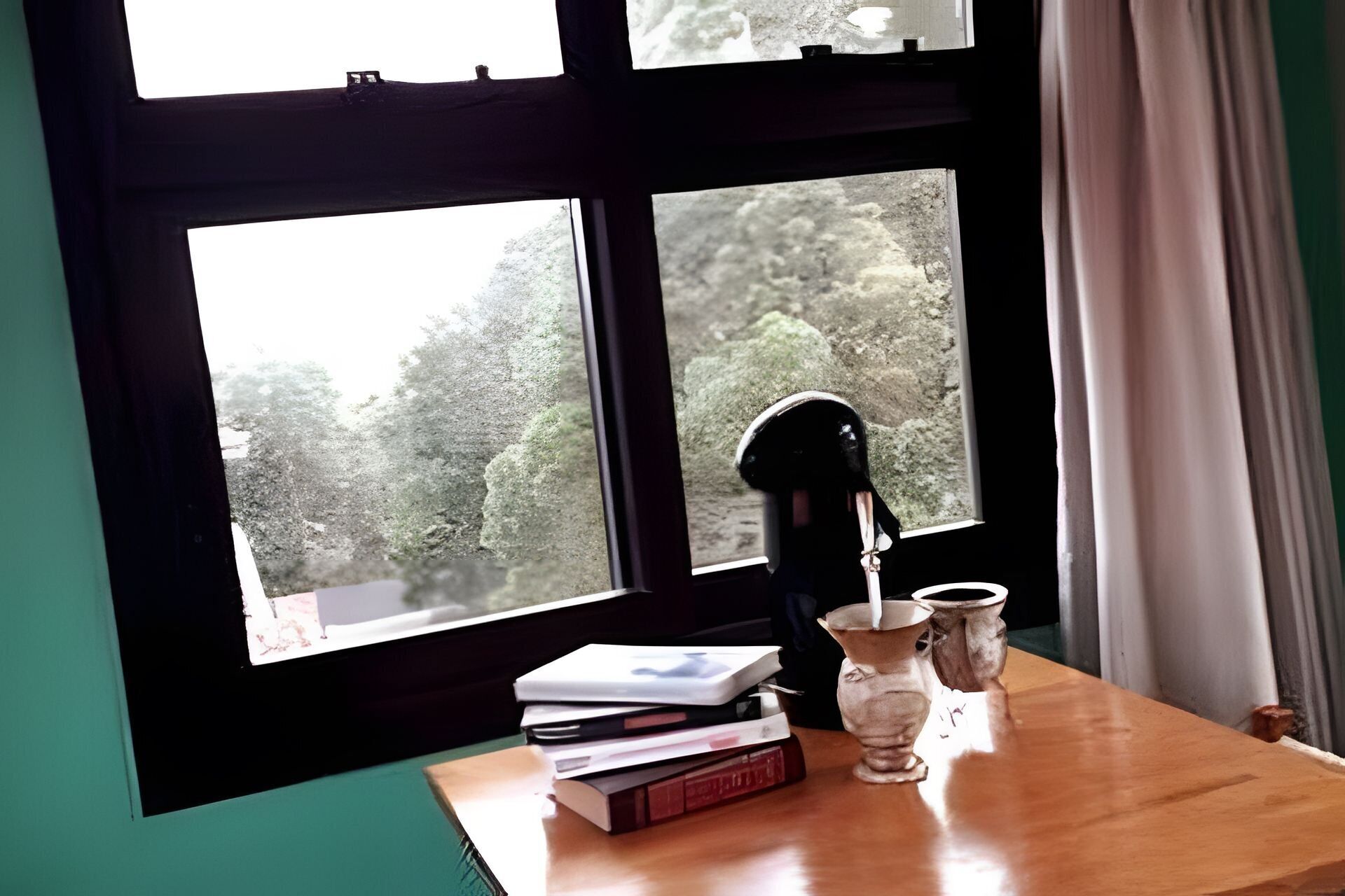 Een houten tafel met een stapel boeken, een glazen vaas en een zwart voorwerp.