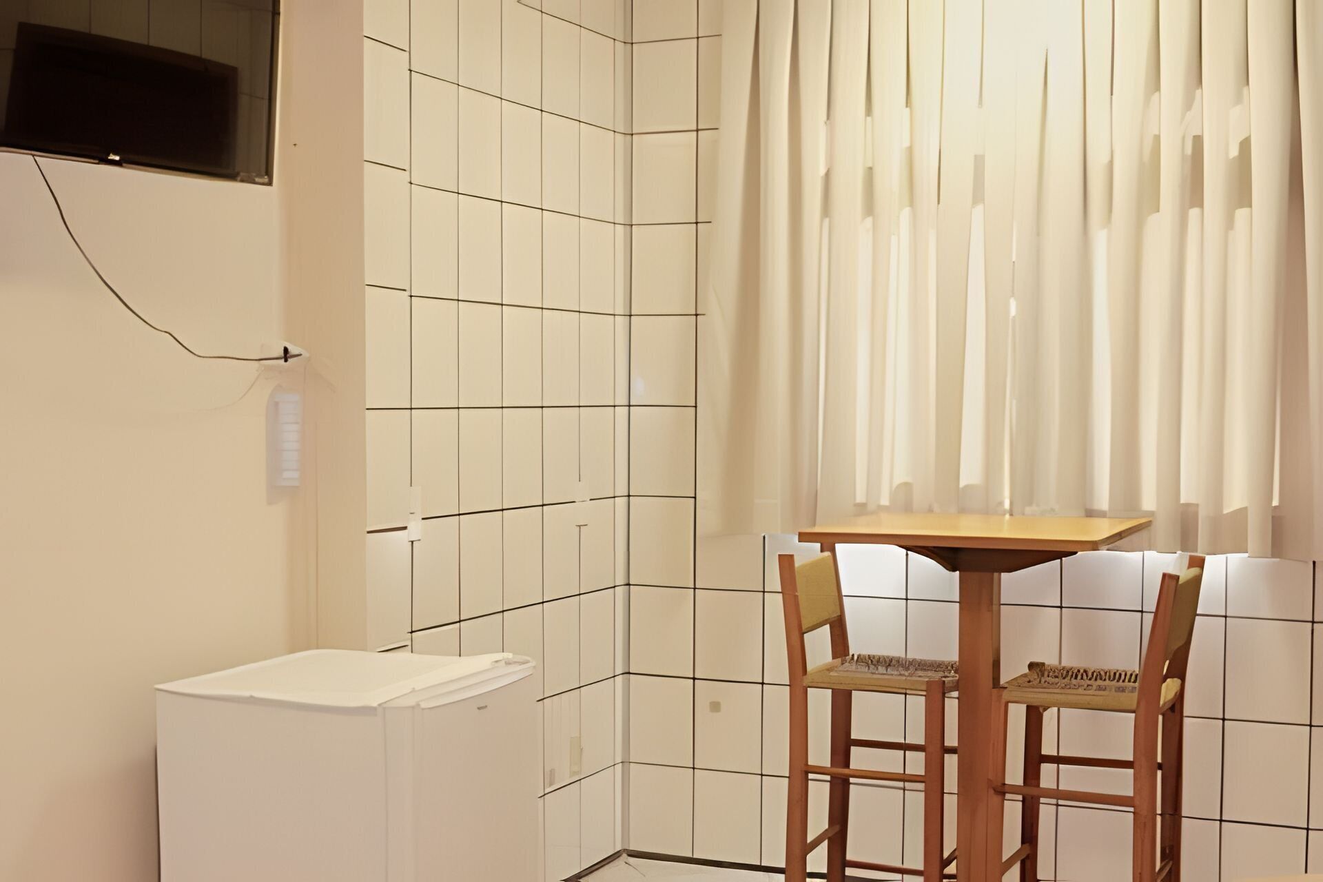 A small kitchenette with a white refrigerator, a wooden table, and two chairs.