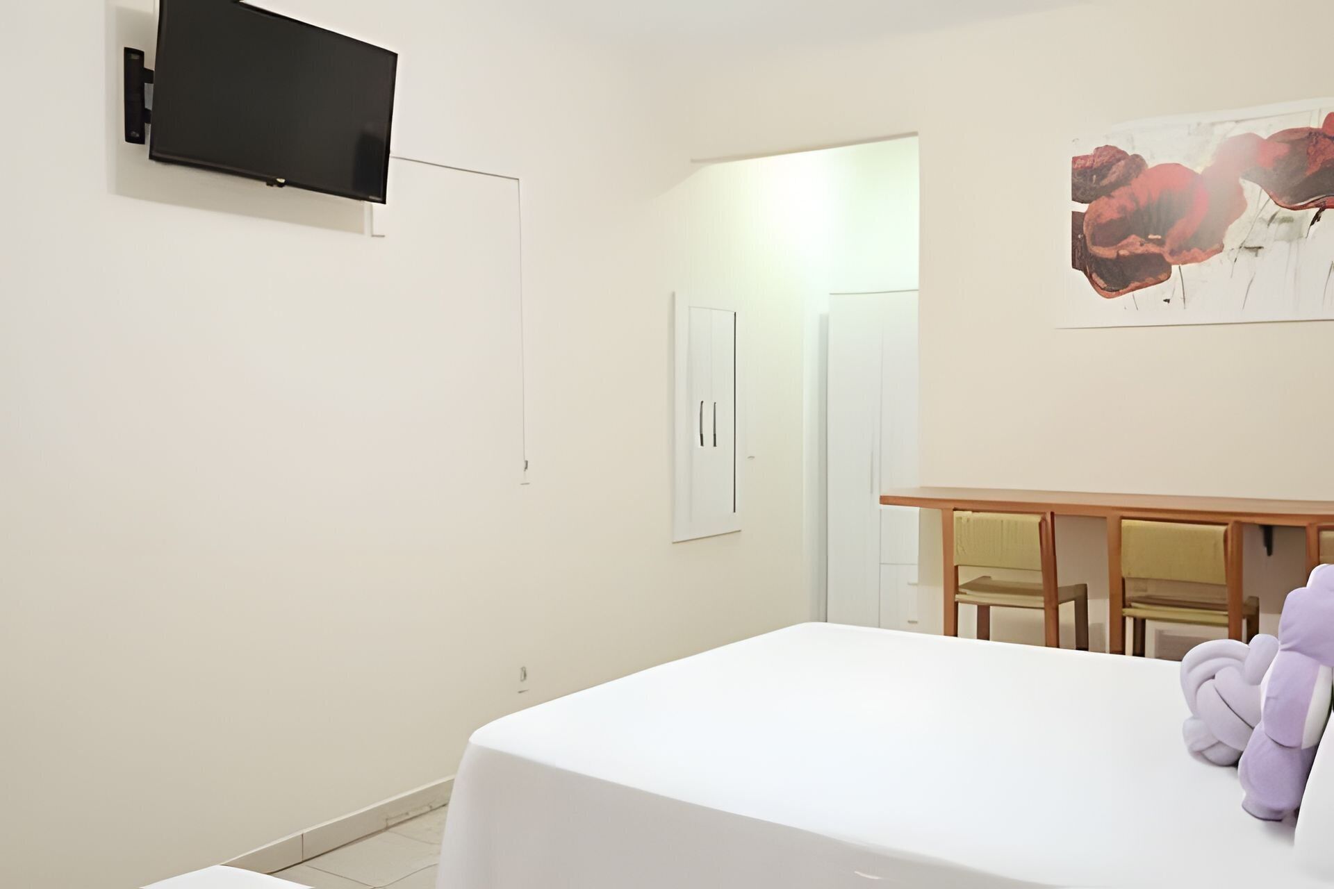 Una habitación con una cama, un televisor en la pared, una puerta y un cuadro.