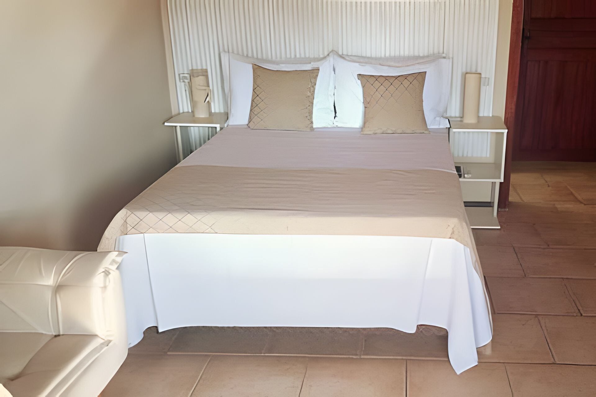 A large bed with a white bedspread and two pillows, flanked by nightstands with lamps.