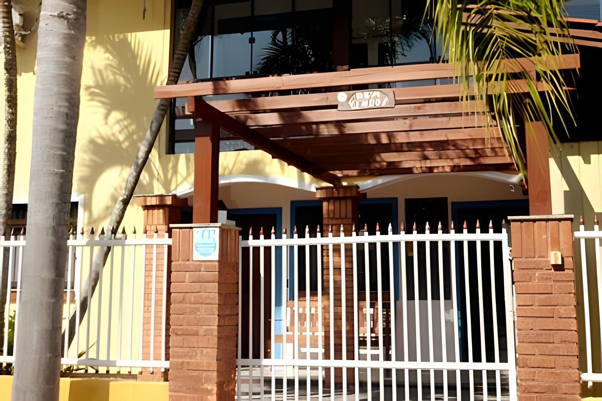 A gated entrance with a wooden pergola, brick pillars, and a white fence.