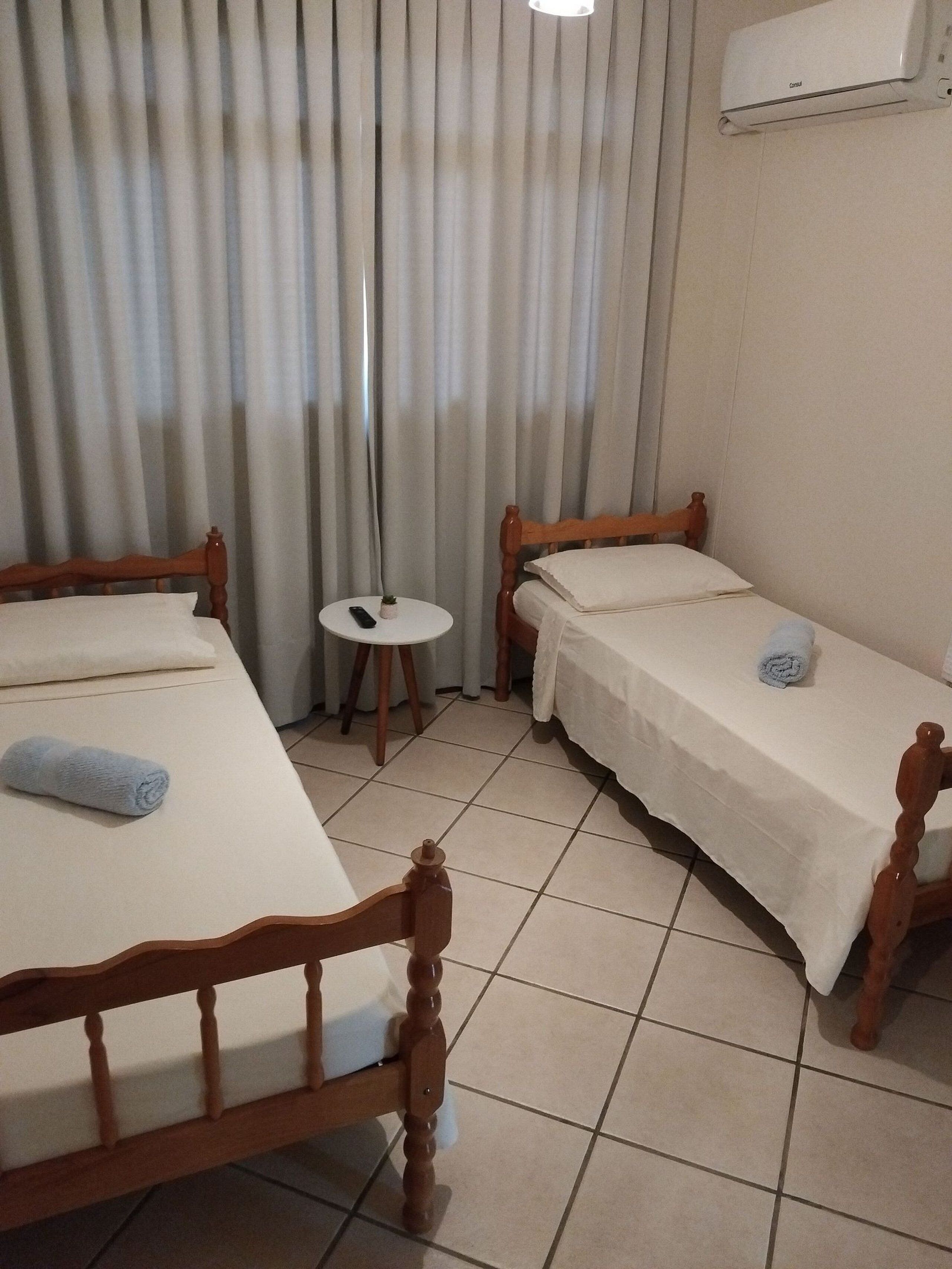 Habitación de hotel con dos camas de madera, una mesita redonda, un control remoto y un equipo de aire acondicionado en la pared.