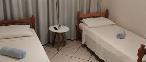 Habitación de hotel con dos camas de madera, una mesita redonda, un control remoto y un equipo de aire acondicionado en la pared.