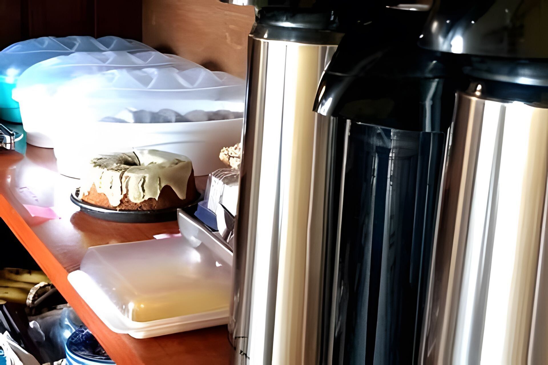 Una encimera de cocina con un pastel, un recipiente blanco y tazas térmicas de acero inoxidable.
