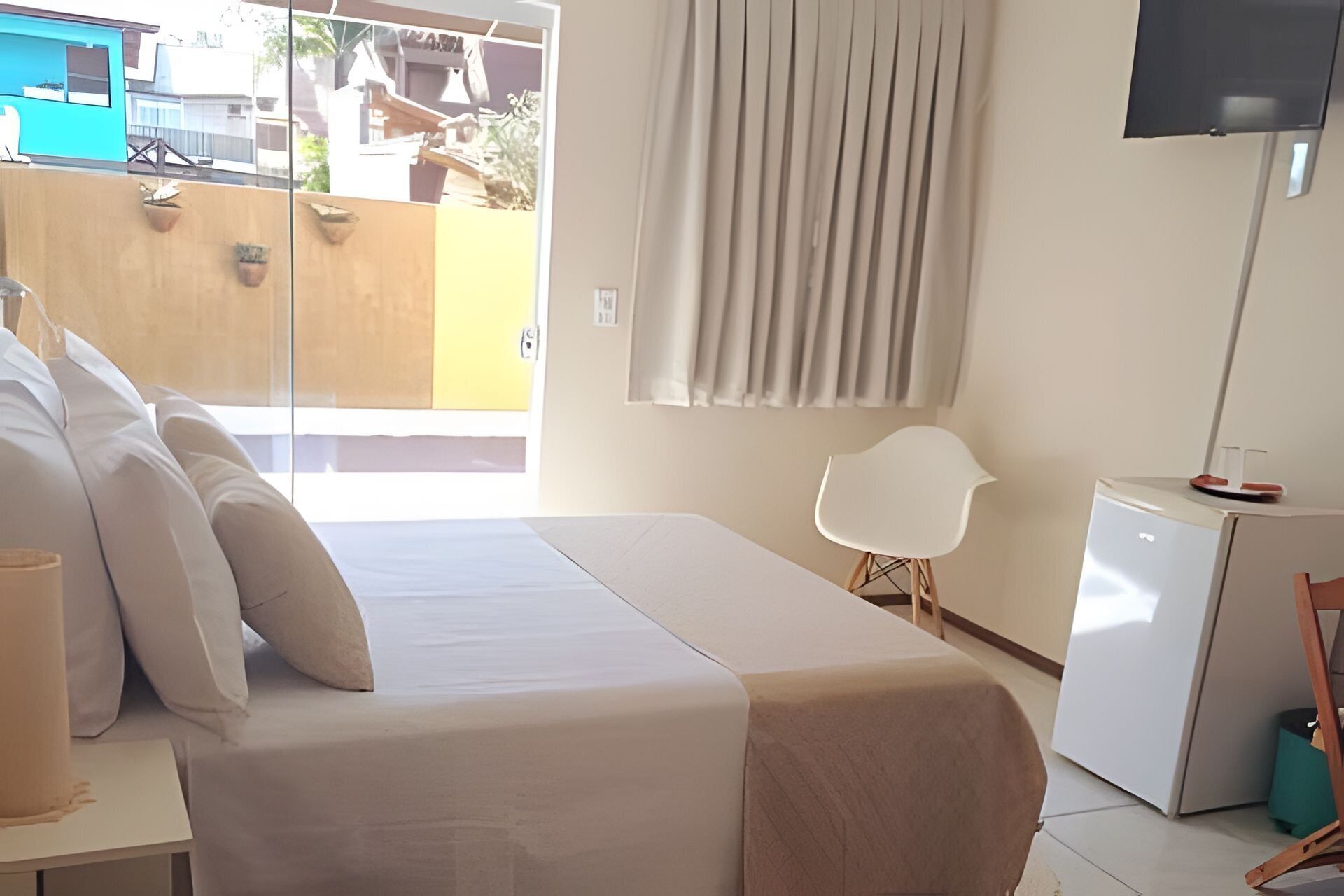 A bedroom with a bed, a desk, a chair, a TV, and a window with curtains.