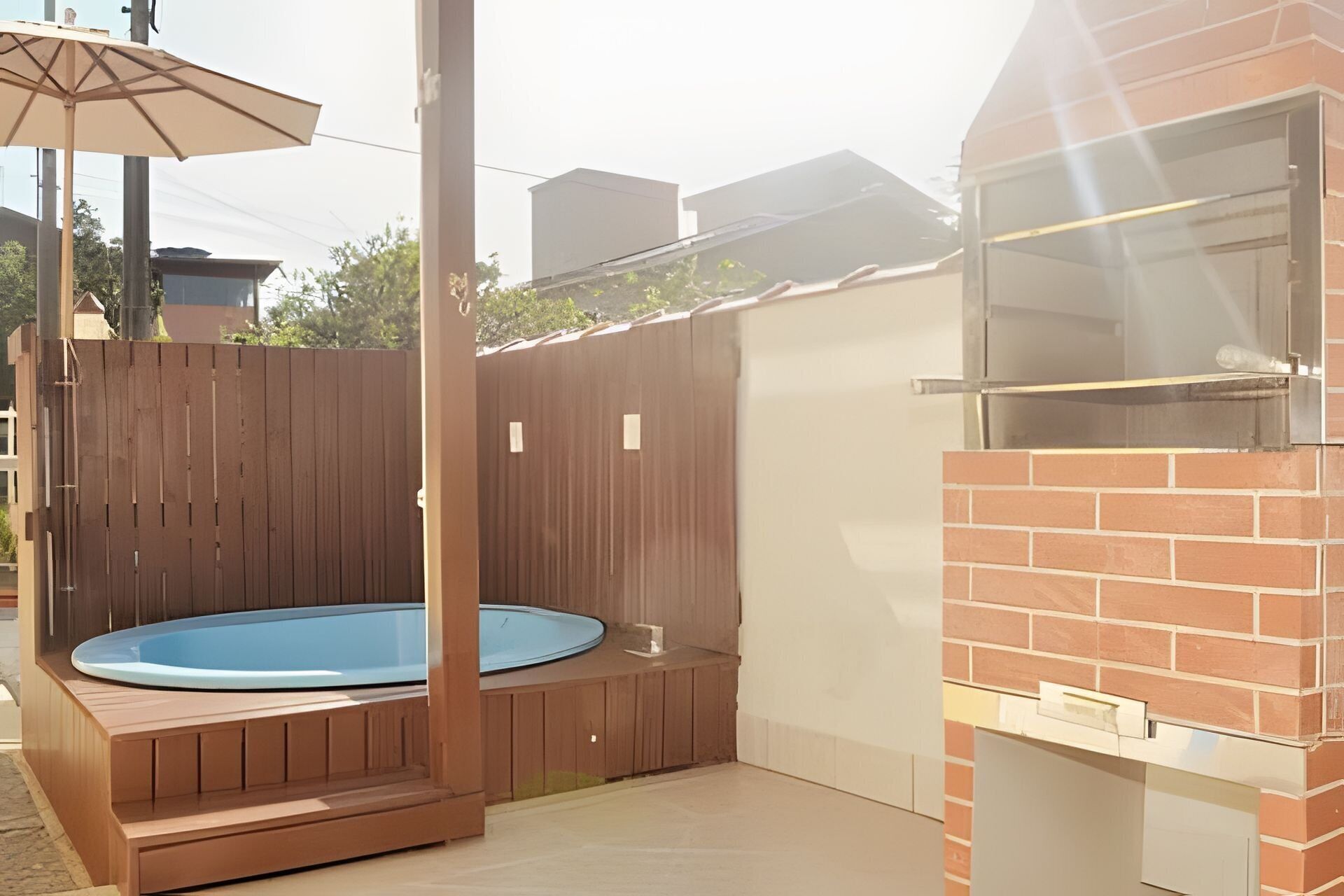 A backyard with a hot tub, a barbecue grill, and a wooden fence.