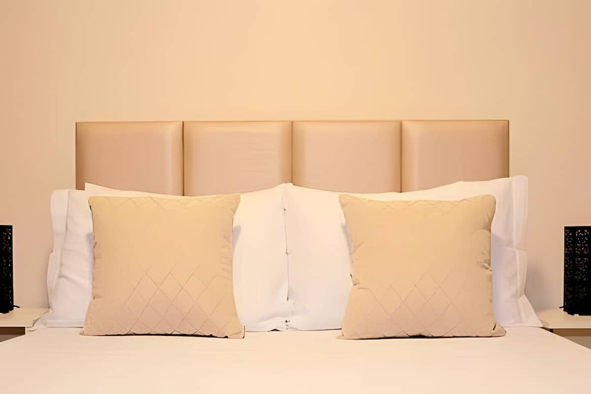 Una cama con cabecera, dos almohadas y una colcha blanca.