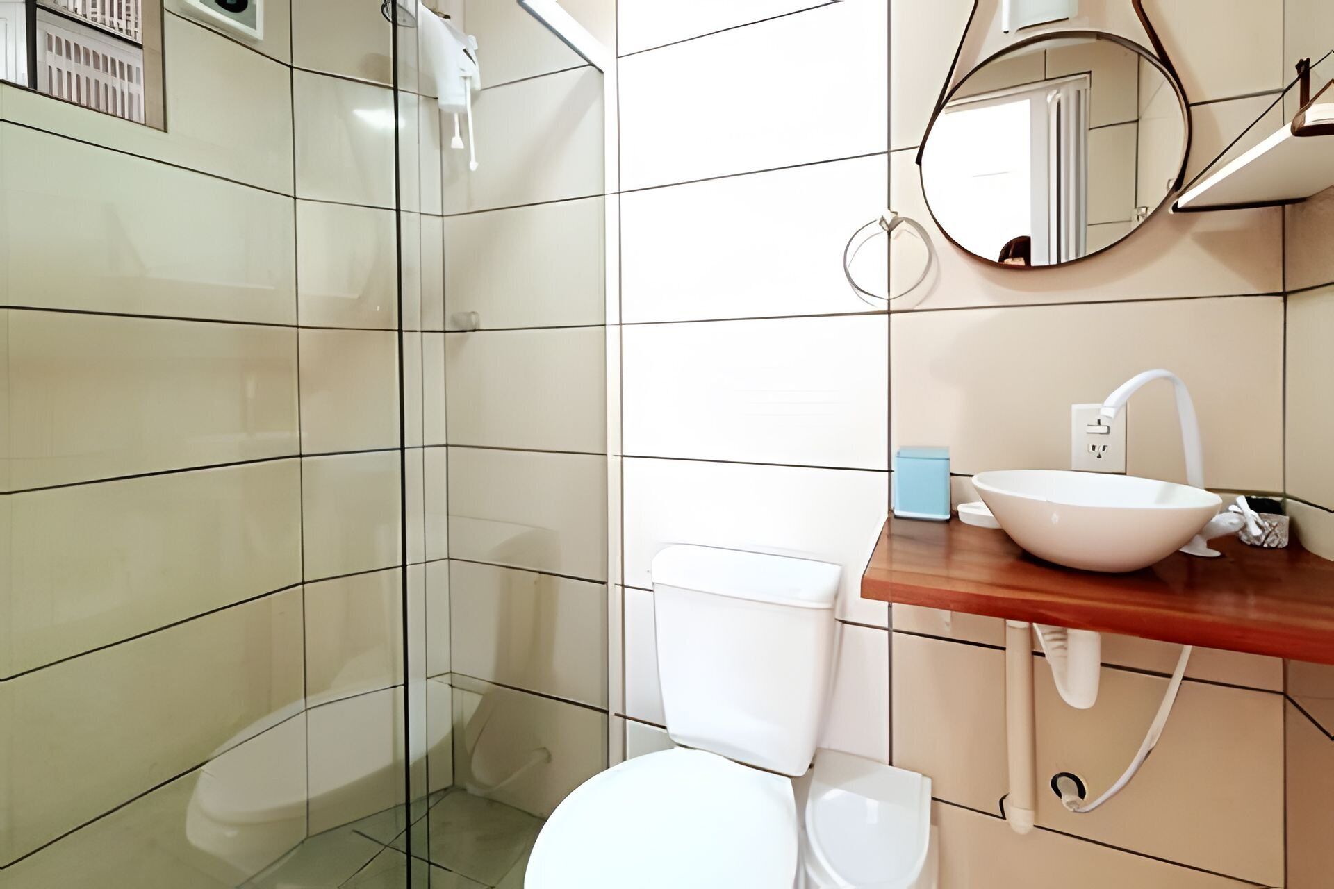 A bathroom with a glass shower enclosure, a white toilet, a sink with a mirror above it, and a blue soap dish.